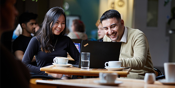 Two students in a coffee shop looking at laptops