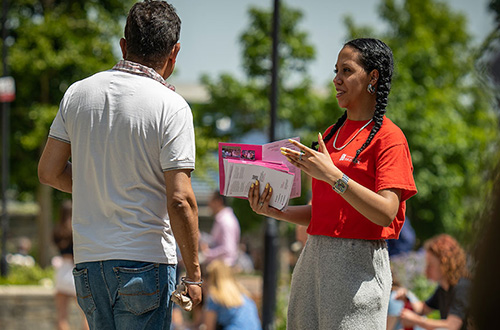 A female student ambassador holding open day guides talking to a guest