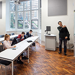Students sat at desks in seminar room with person speaking at the front of the room