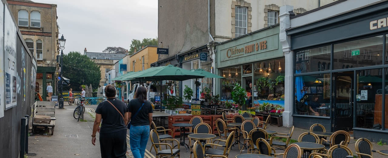 people walking past outdoor seating and coffee shops in clifton village