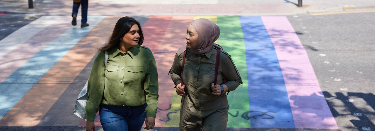 Two students crossing the street on a rainbow painted zebra crossing.
