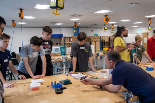 A group of Sixth Form students are talking with current CDT students about the NextCOMP Crusher, a device that is used to test the integrity of a composite of jelly and dried pasta noodles.