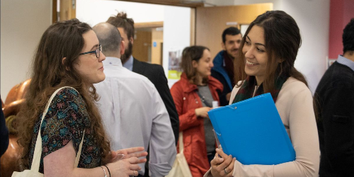 Two women talking at a conference gathering, select to go to the work with us web page.