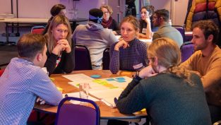 PhD students sitting around a round table discussing wellbeing challenges 