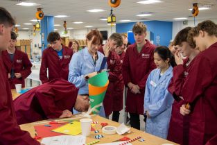 KLB students, staff and volunteers gather round a table as a group tests their marble run creation