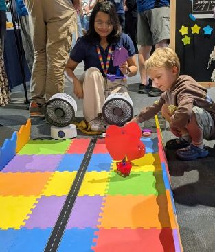 A staff member and young boy look on as his sail car creation races down the multicoloured race track
