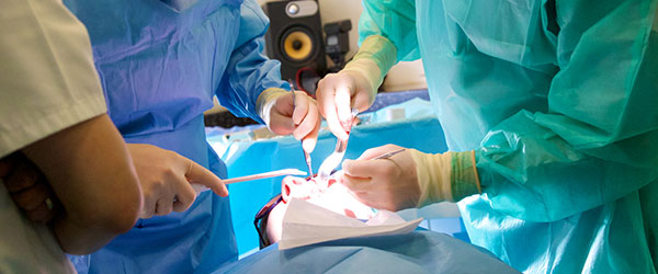Surgeons operating on dental patient underneath an overhead lamp.
