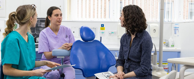 A patient talking to two dental professionals in a dental treatment room