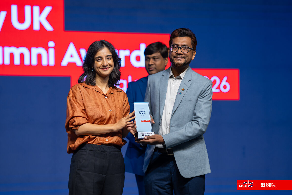 A woman in an orange blouse handing an award to a man with glasses in a blue suit.
