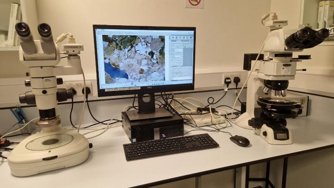 There is a PC with a monitor on a lab bench, on either side is a microscope. The PC screen shows an image of a geological thin section.