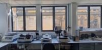 This is a photograph of a lab white lab bench, with large windows behind it. On the bench are two polishing machines, an auto grinder and a thin-sectioning machine.
