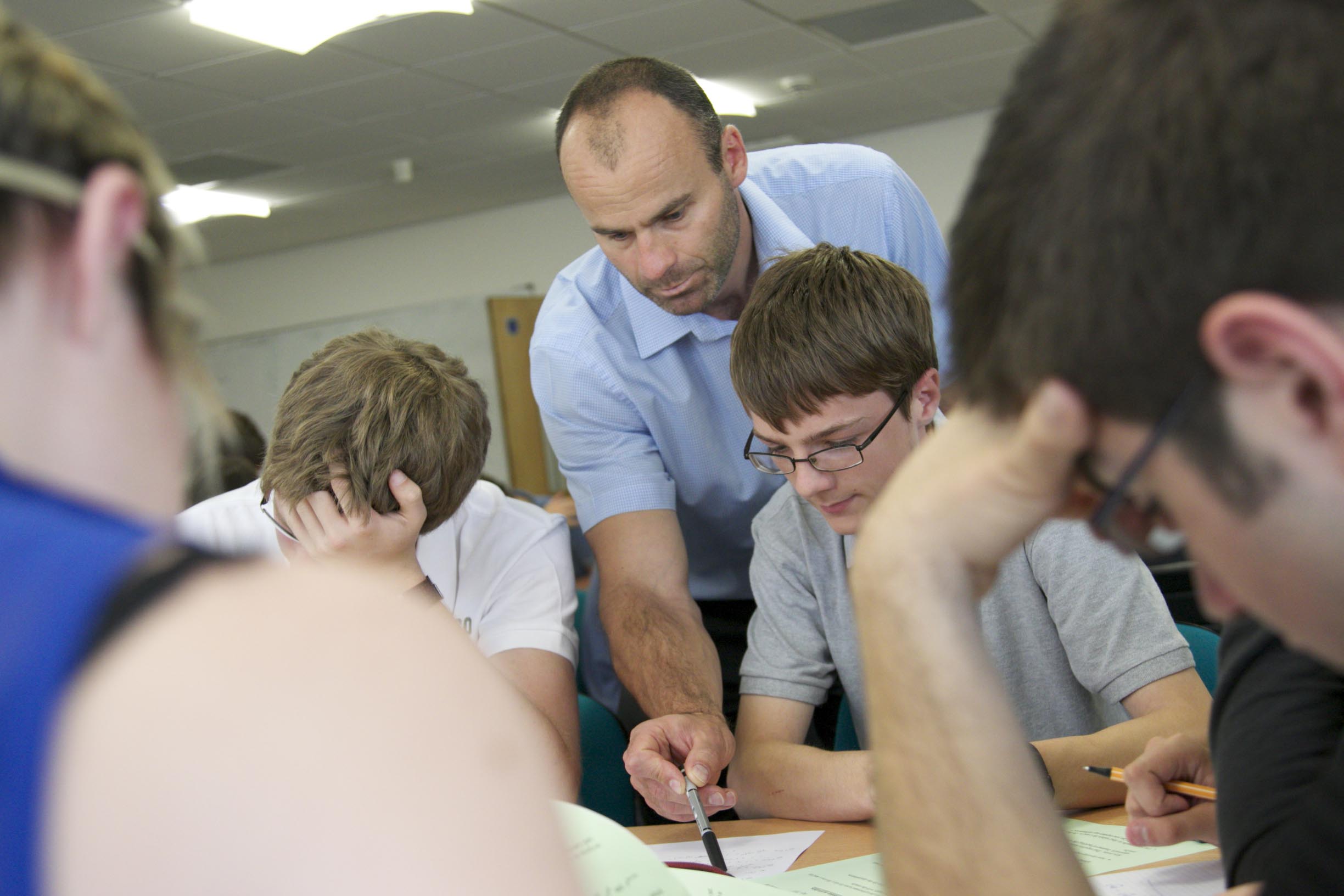 A male teacher leans over the shoulder of a student to help