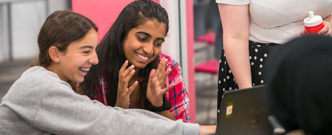 Two girls laughing and pointing while working at a laptop