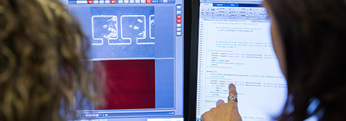 Two women in front of screens showing code