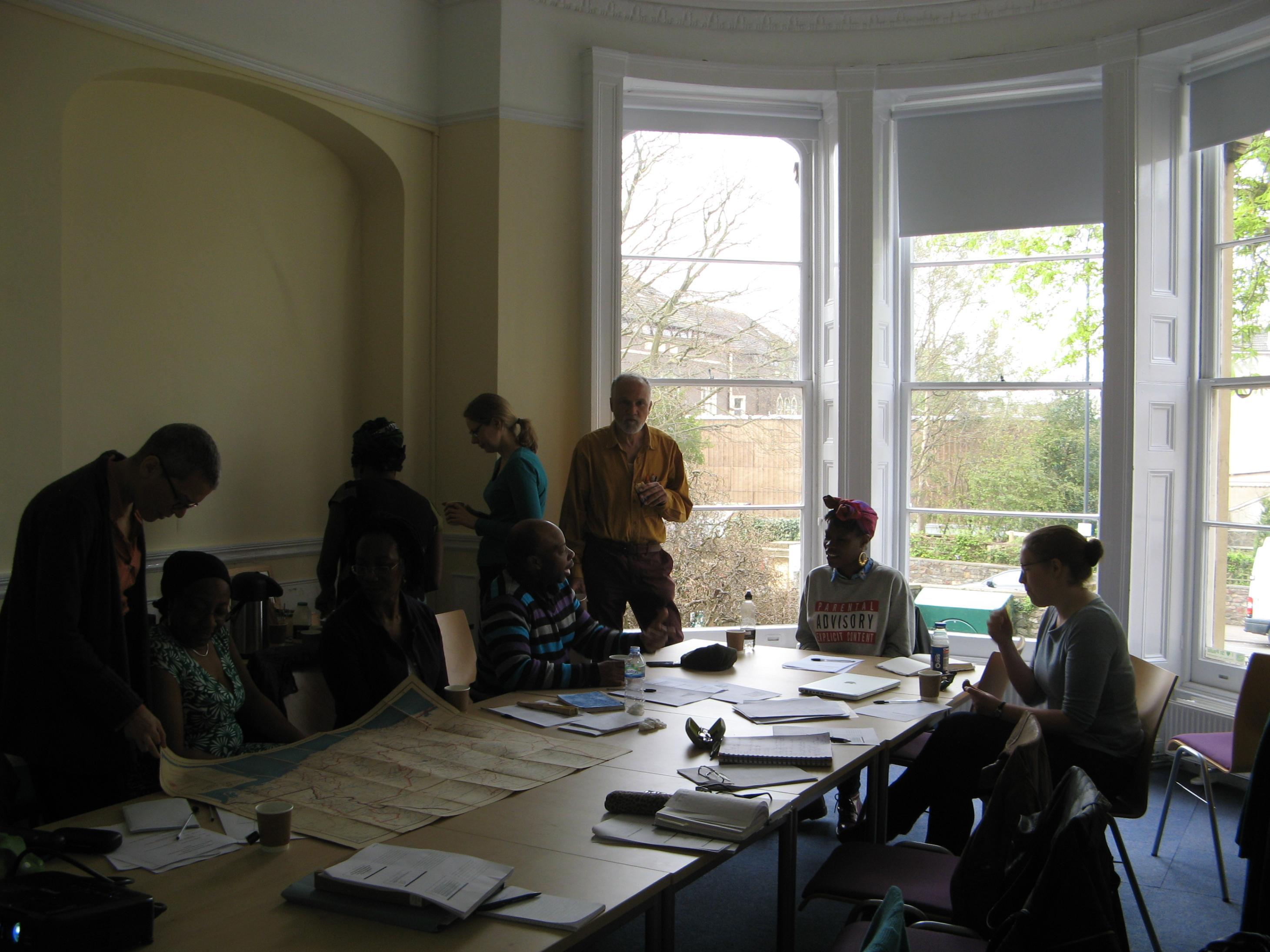 Photograph of people in a seminar room with papers laid out on the table and a bright window