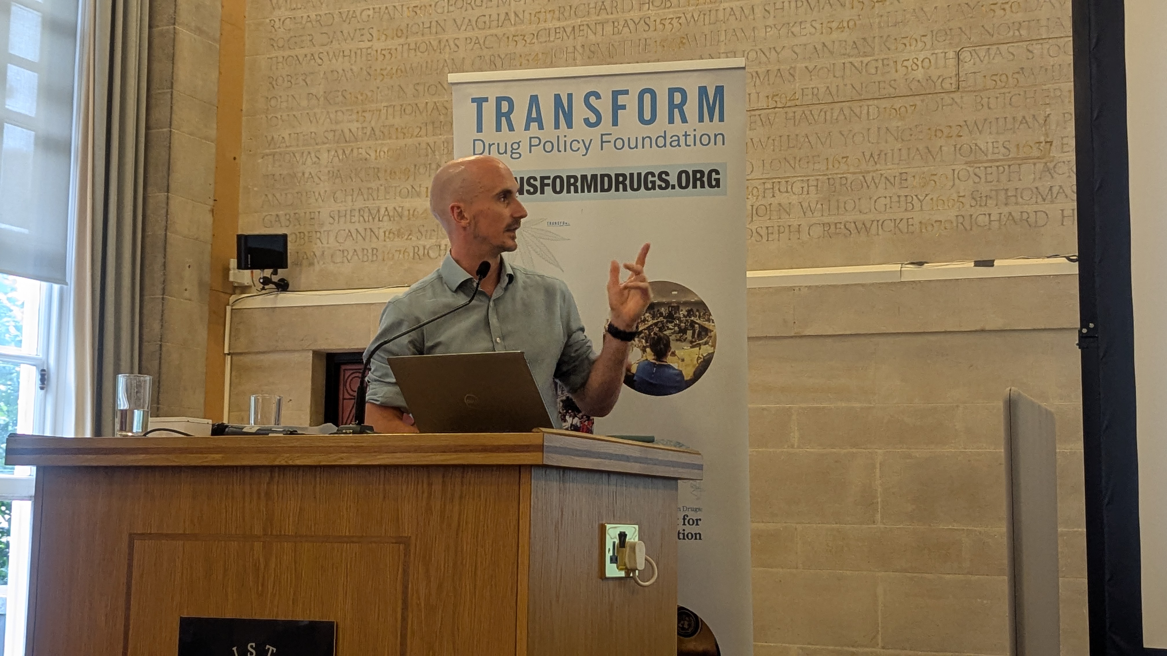 Dr Adam Holland standing behind a podium, mid-speech
