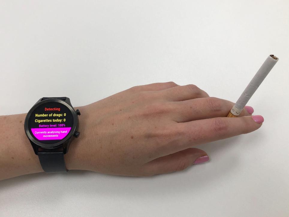 A photo of a smartwatch on someone's hand holding a cigarette, displaying text that counts the amount of times the person has smoked that day
