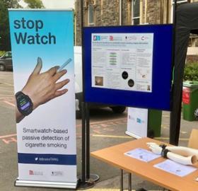 An outdoors display of the Stop Watch smoking cessation app. It features a large banner with a picture of a hand holding a cigarette and a watch on their wrist. The banner reads 