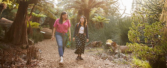 Two people walking and smiling. They are surrounded by trees and greenery.