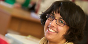 A woman with dark hair and glasses smiling.