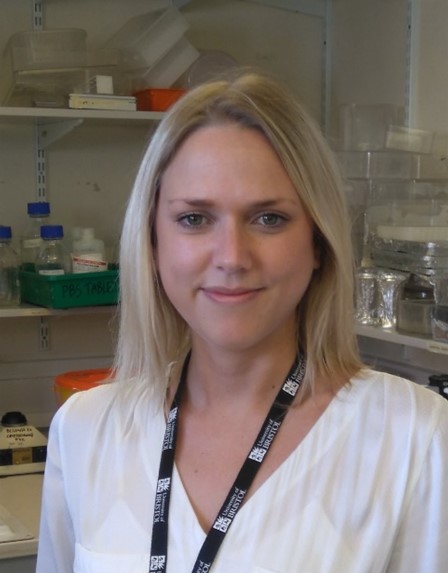 Headshot of woman standing in front of a laboratory. 