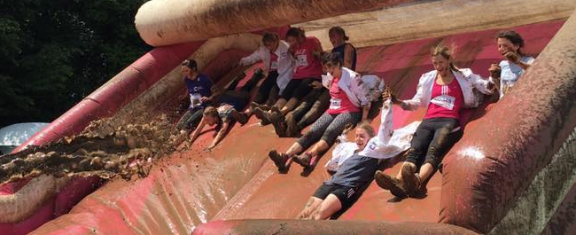 An image of a group sliding down a muddy inflatable