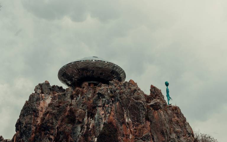 An image of a UFO on top of a mountain next to an alien
