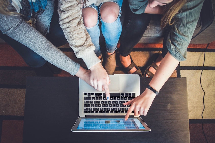 A group of people pointing to a laptop screen.