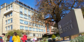 People in brightly coloured jumpers by a 'University of Bristol' sign, outside a building.