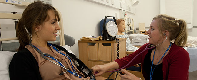 Woman measuring another woman's blood pressure using manual pump and stethoscope 