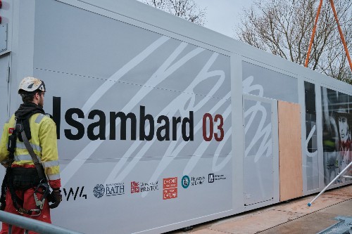 A man in a hi-viz jacket and helmet standing next to a sign with the words Isambard 03