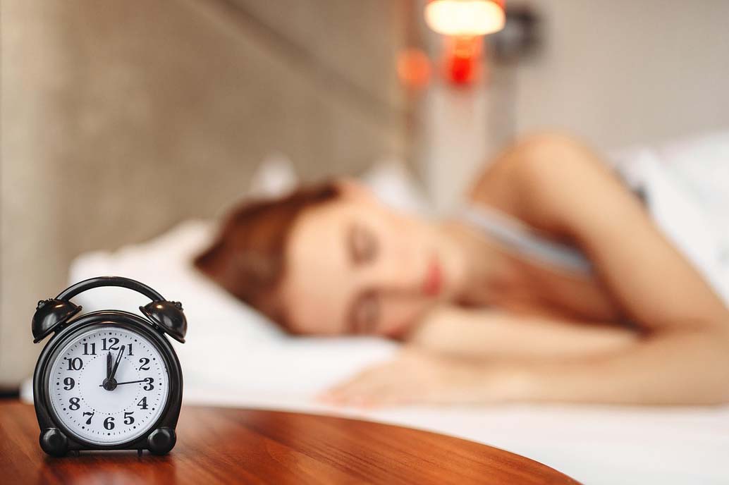 A women sleeping with an alarm clock on a bedside table