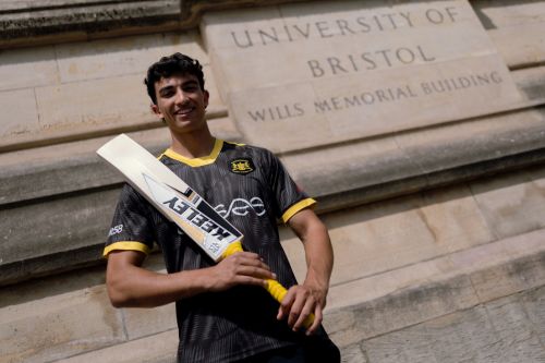 Photograph of Kamran Dhariwal holding a cricket bat stood outside the Wills Memorial Building