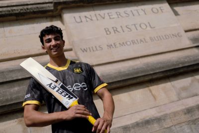 Photograph of Kamran Dhariwal holding a cricket bat stood outside the Wills Memorial Building