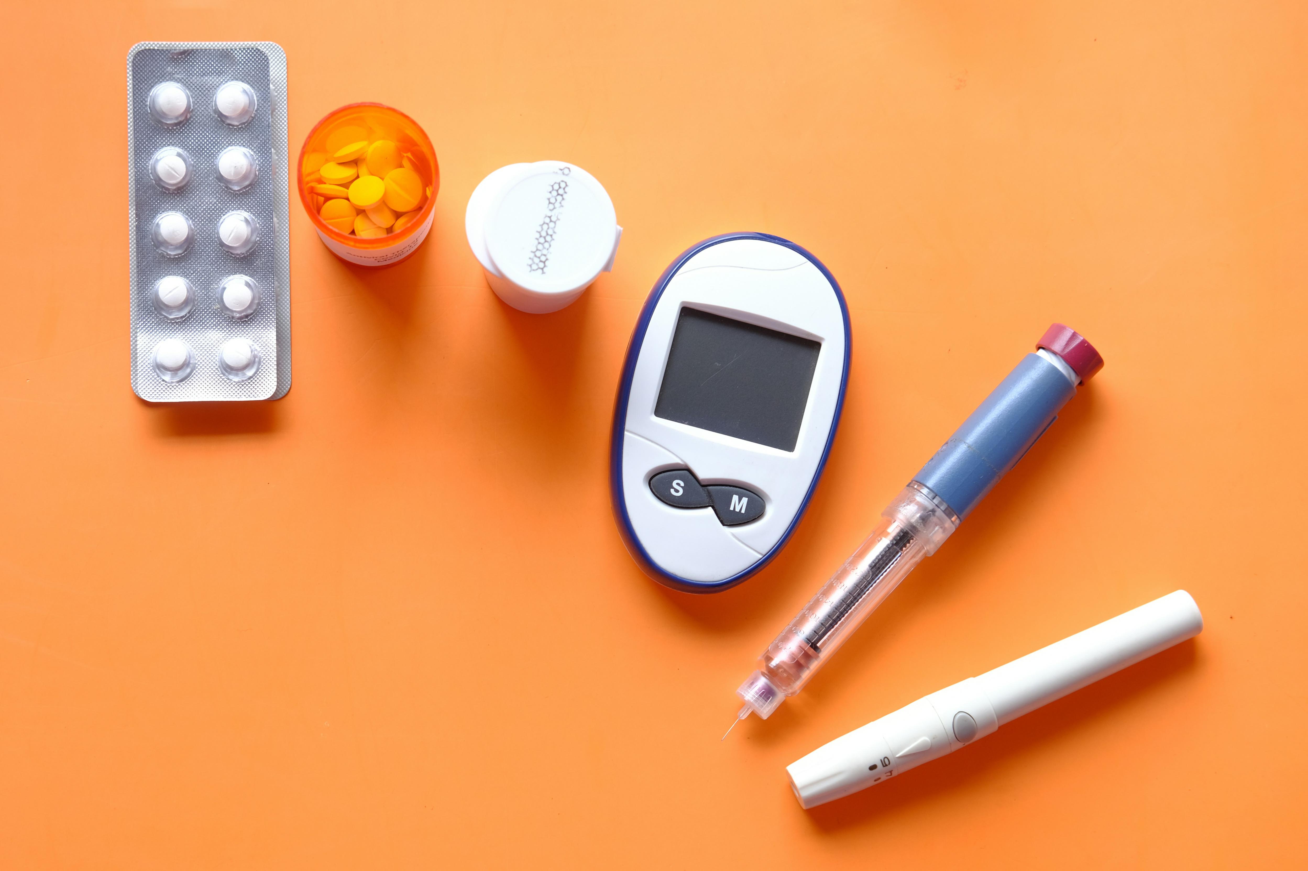 Unsplash image of an insulin pen, diabetic measurement tools and pills on orange background