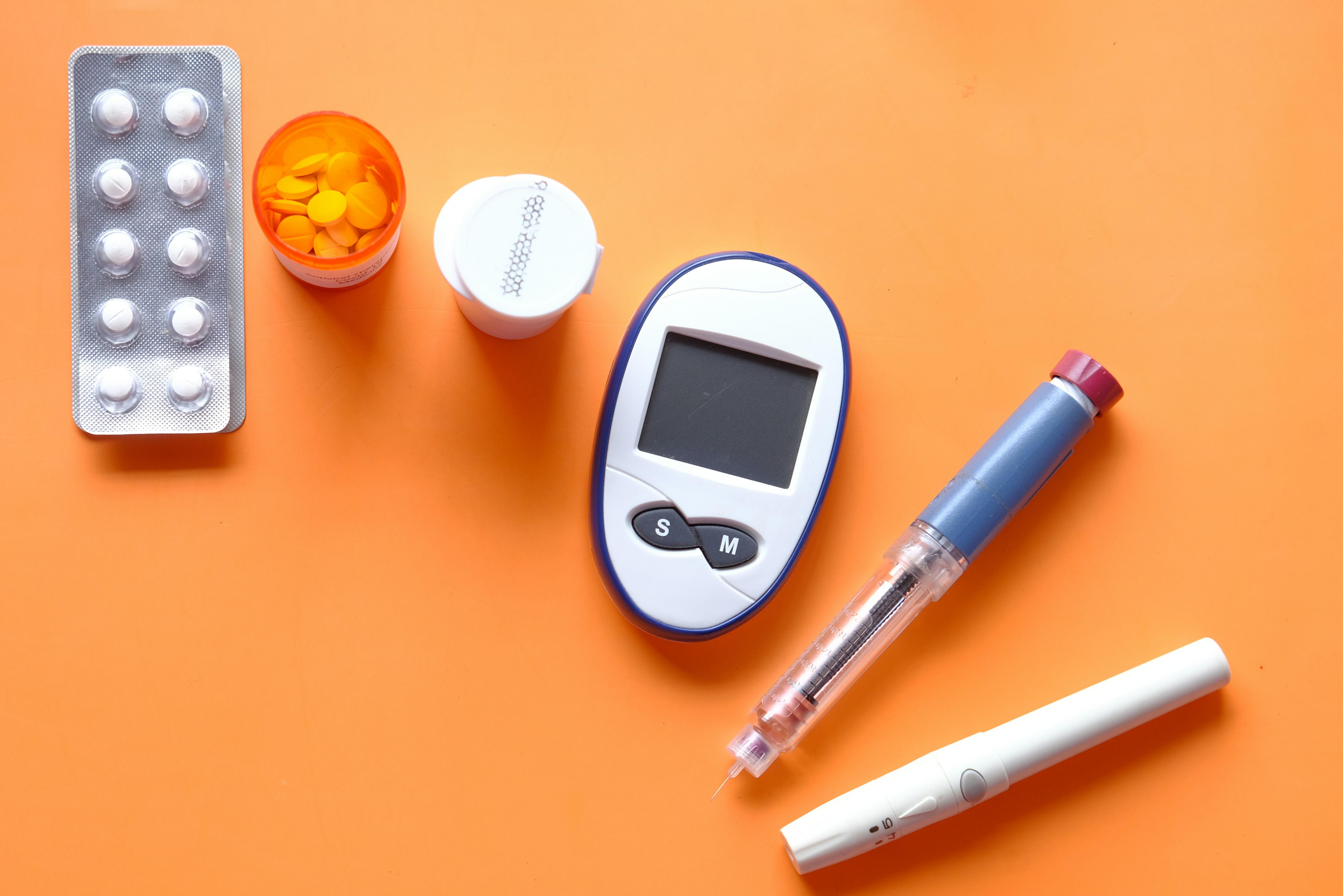Unsplash image of an insulin pen, diabetic measurement tools and pills on orange background