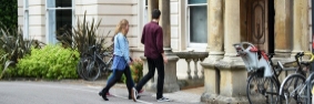 A female student and a male student walk into the Philosophy department building, which has bicycles parked outside. 