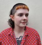 A woman wearing a red patterned shirt with short dark hair and an auburn fringe