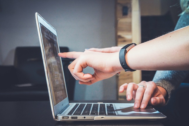 Two pairs of hands pointing at a laptop screen.