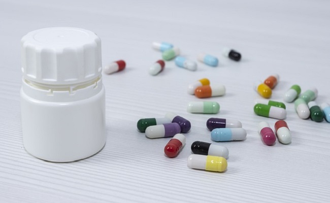 Assortment of pills scattered on table next to a white pill box.