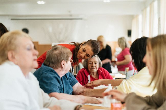 Care home residents sitting around table speaking to care home worker.