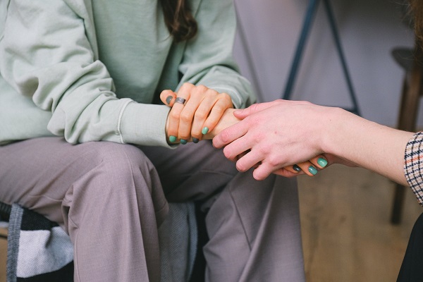 Two seated people holding hands in a gesture of comfort/support.