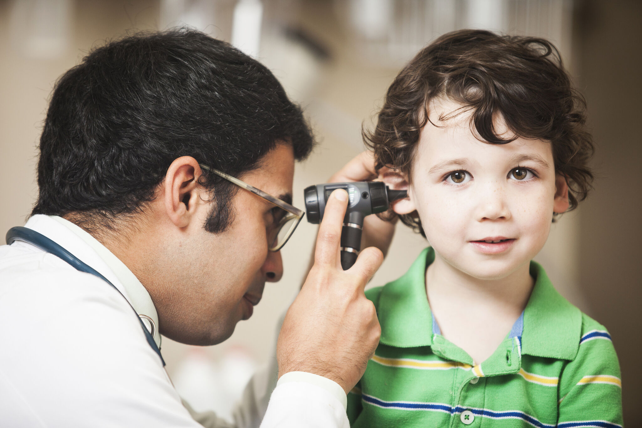 GP uses a medical instrument to see inside a young child's ear.