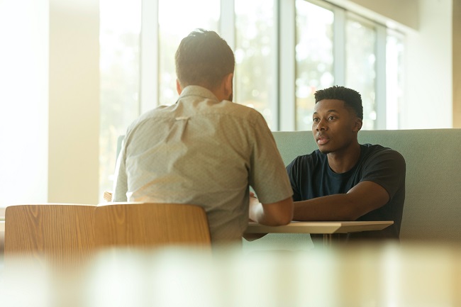Young Black man seated at table talking with older white man