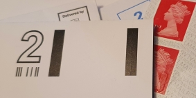 Image showing different types of postage, with some franked envelopes on top of a partially used sheet of 1st class orange stamps behind