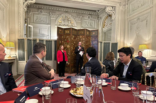 A woman and a man are standing on a stage in front people sat at tables