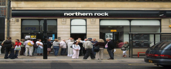 people walking on the pavement in front of a northern rock bank
