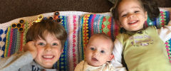 Three children lying on a multi coloured mat