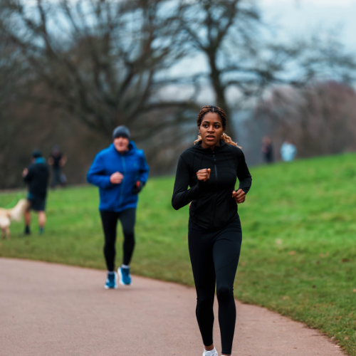 A female runner running on a path next to some grass. There are other runners in the background
