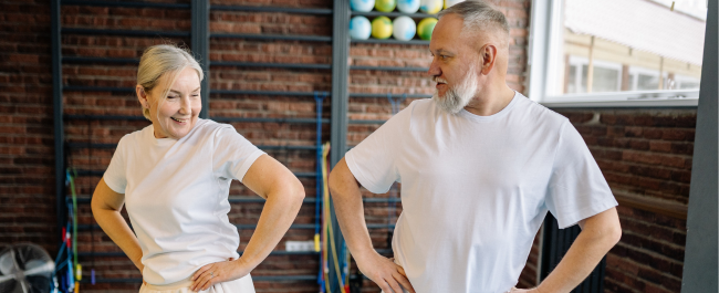 A female and male looking at each other while standing side by side with their hands on their hips.